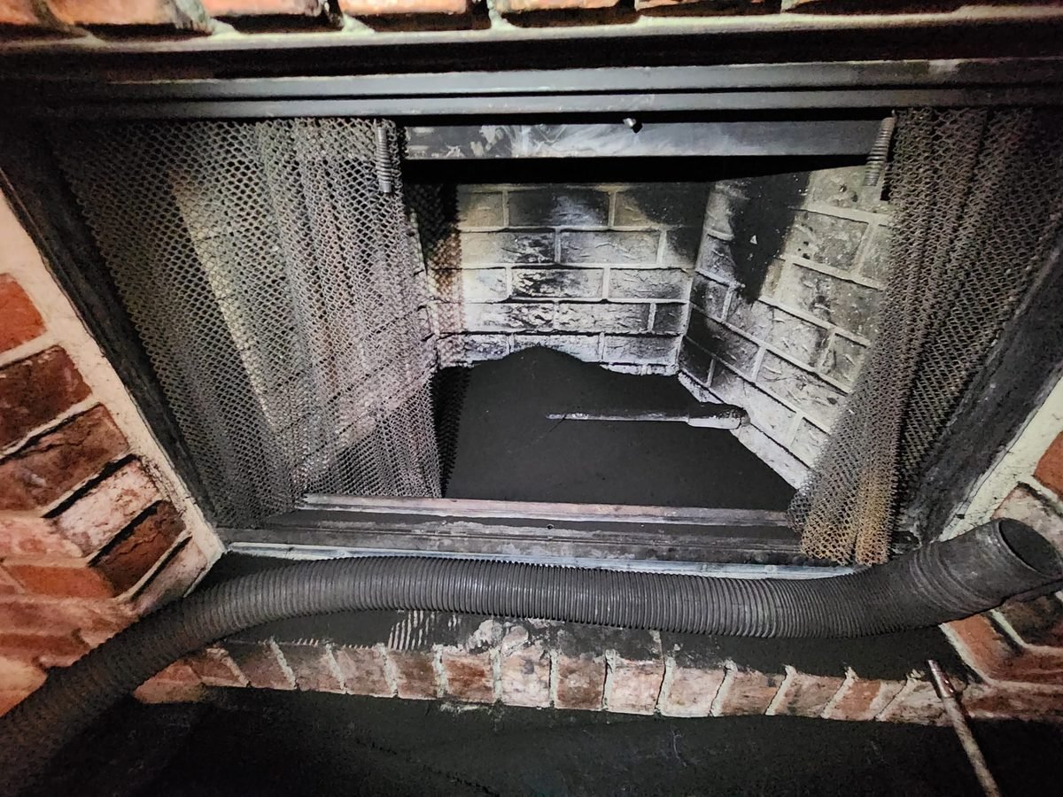 The inside of a heavily sooted firebox with a vacuum hose fed through the opening