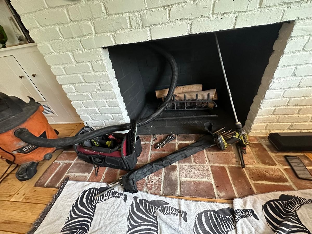 Sweep rods and a vacuum hose laid across the hearth of a whitewashed brick fireplace, with drop cloths down