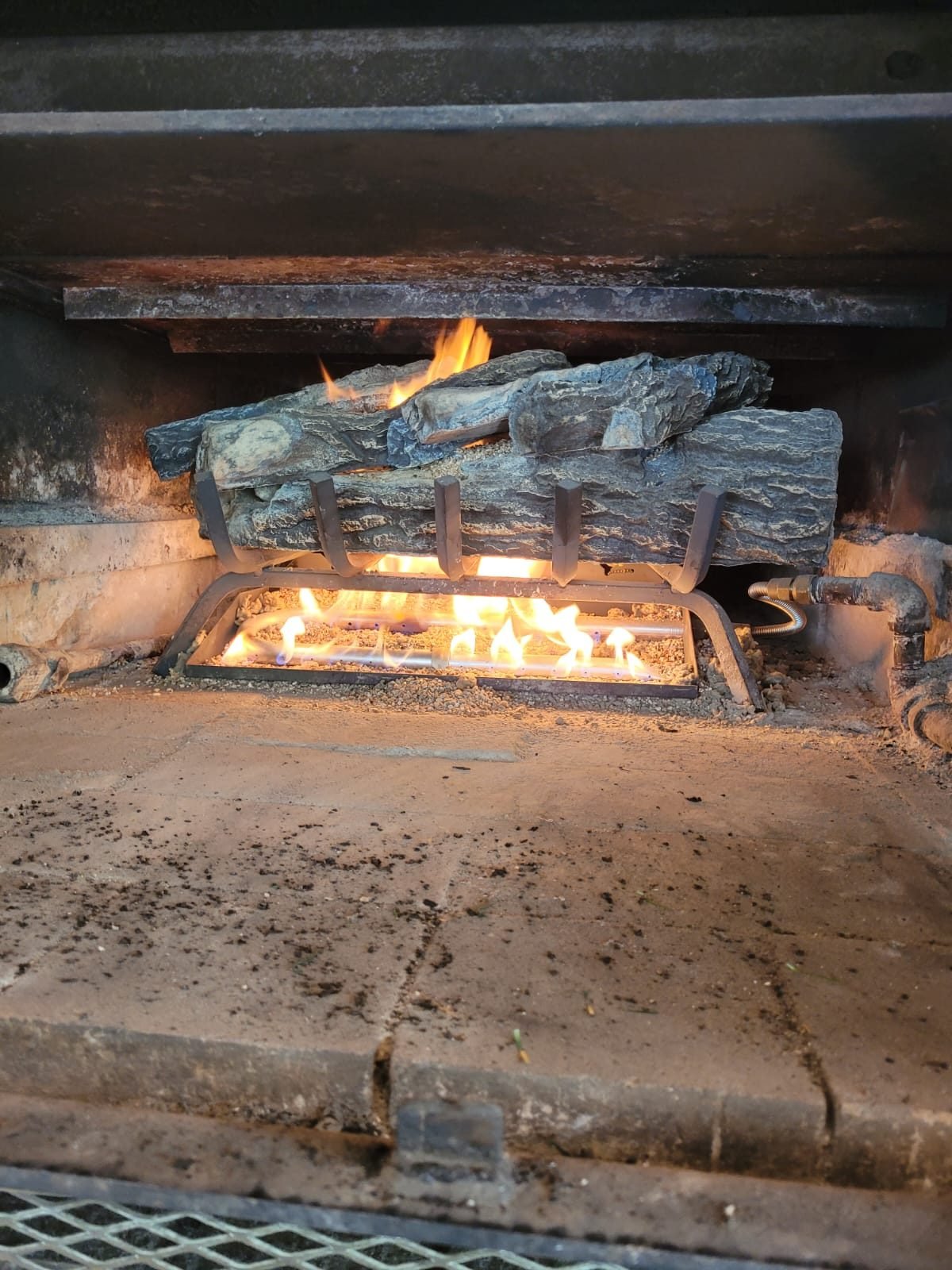 Close view of a gas fireplace burner with an even flame running under a ceramic log set
