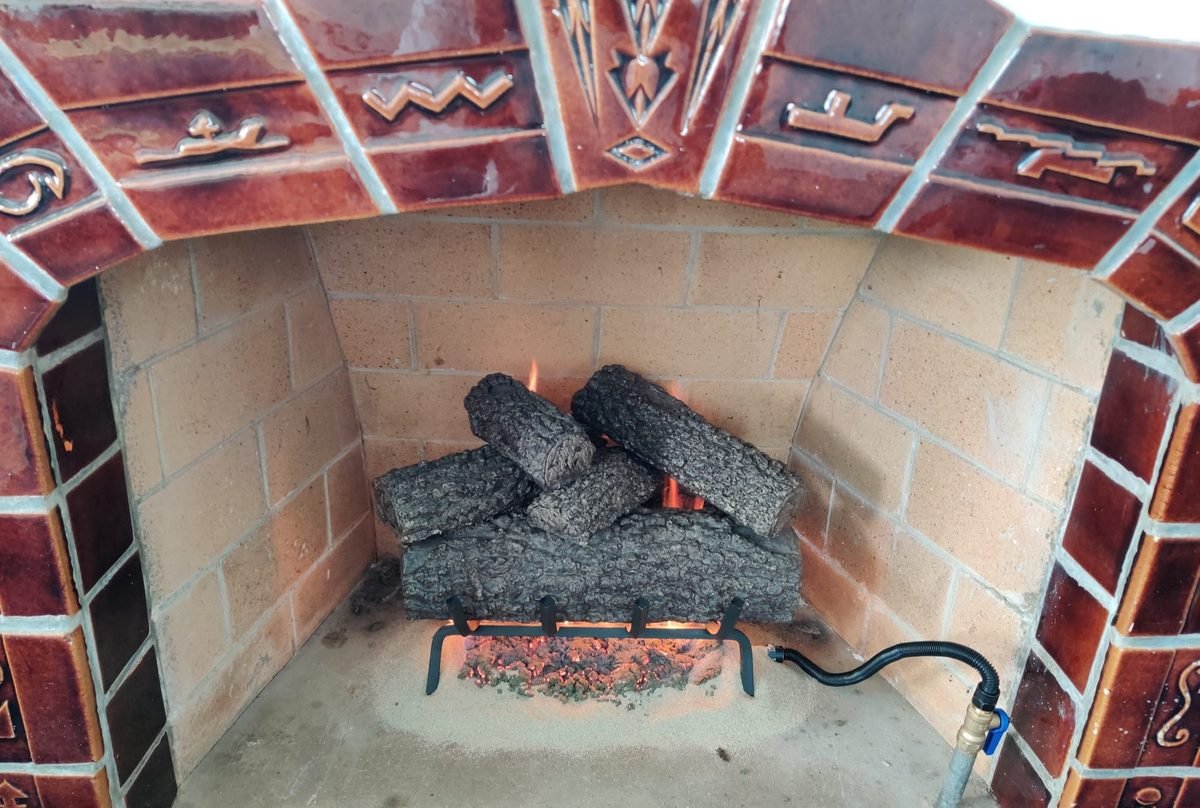 A decorative tiled fireplace surround with a gas log set burning in the firebox