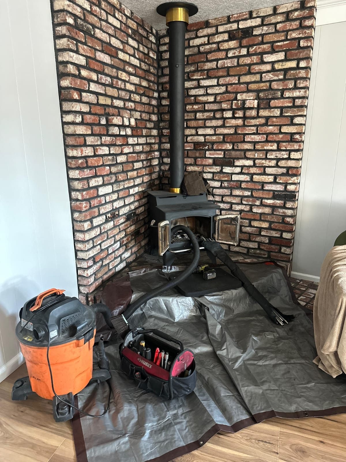 A freestanding wood stove in a brick alcove with tarps laid out and service equipment alongside it